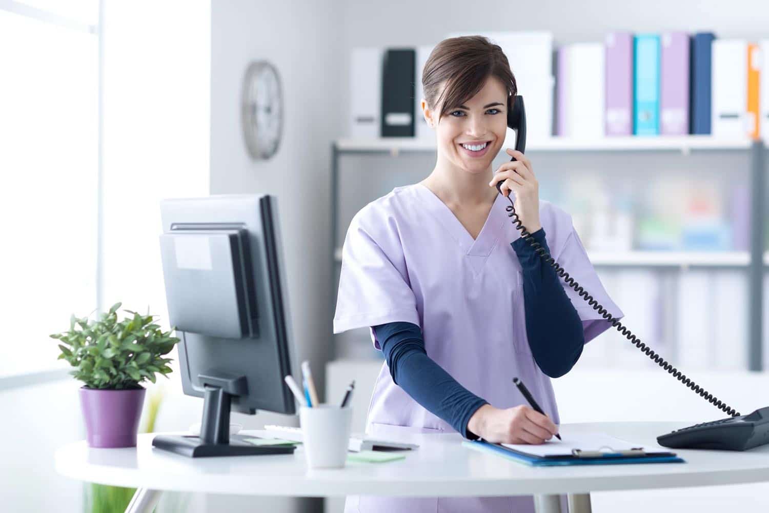 Beautiful nurse speaking on the phone and writing on a clipboard